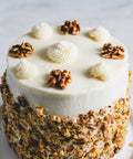 Banana walnut cakewith decorative swirls of frosting and whole walnuts, rolled in crushed walnuts.