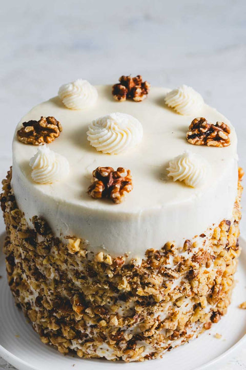 Banana walnut cakewith decorative swirls of frosting and whole walnuts, rolled in crushed walnuts.