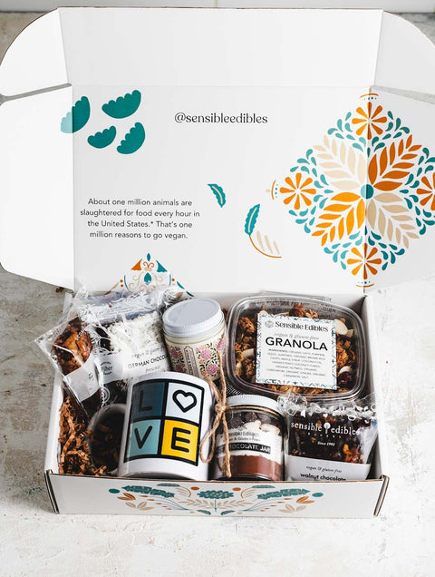 Gift box opnened to show contents: a jar of hot chocolate mix, walnut chocolate brownie, sensible edibles mug, candle, granola, and german chocolate brownie. The box is white with a floral background