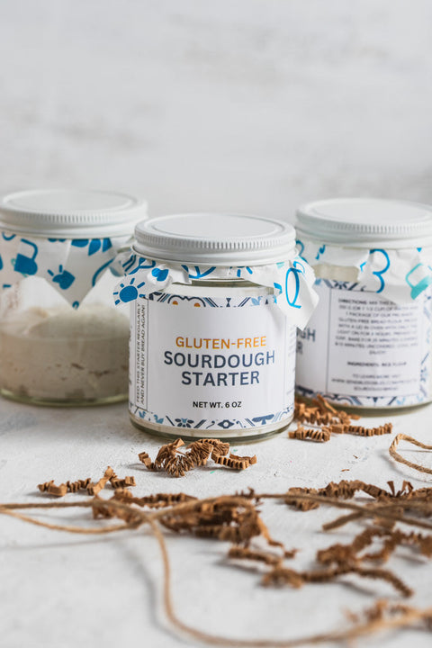 Three jars of gluten-free sourdough starter on a white table with decorative fabric lids.