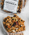 Open container of granola with oats, pumpkin seeds, almonds, and cranberries with more containers in the background
