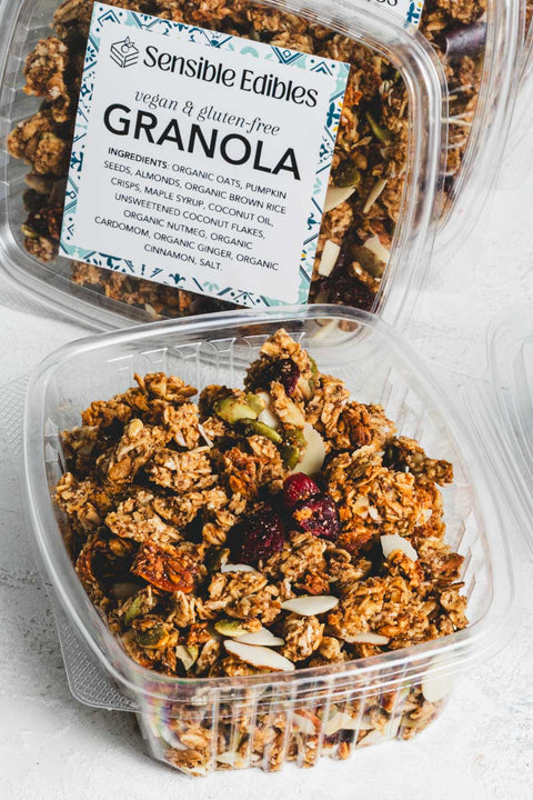 Open container of granola with oats, pumpkin seeds, almonds, and cranberries with more containers in the background