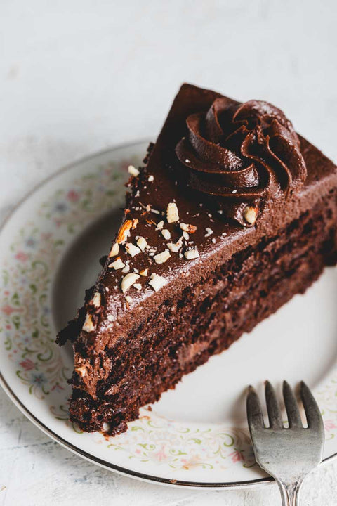 A slice of keto chocolate cake with rich chocolate frosting and chocolate crumble and nut decoration
