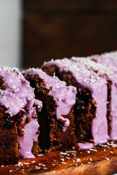 close up of slices of a coconut loaf with blueberries throughout and a vibrant purple blueberry icing garnished with shredded coconut