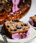 close up of slices of a coconut loaf with blueberries throughout and a vibrant purple blueberry icing garnished with shredded coconut