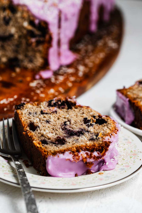 close up of slices of a coconut loaf with blueberries throughout and a vibrant purple blueberry icing garnished with shredded coconut