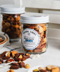 Jars of salted mixed nuts with more nuts piled around them