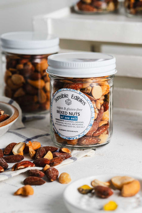 Jars of salted mixed nuts with more nuts piled around them