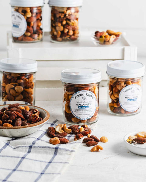 Jars of salted mixed nuts with more nuts piled around them