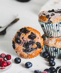 Vanilla berry muffin topped with powdered sugar and mixed berries, resting on its side with more muffins and berries in the background.