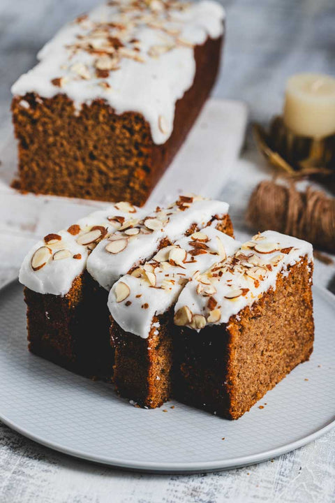 Sliced lemon almond loaf cake with white frosting on top, garnished with almonds, on a plate with a napkin and a candle in the background.