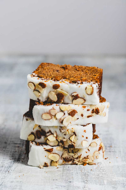 stacked slices of lemon almond loaf with frosting and sliced almonds on top