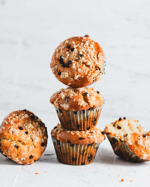 Stack of chocolate chip muffins with a crumb topping, arranged on a light surface.