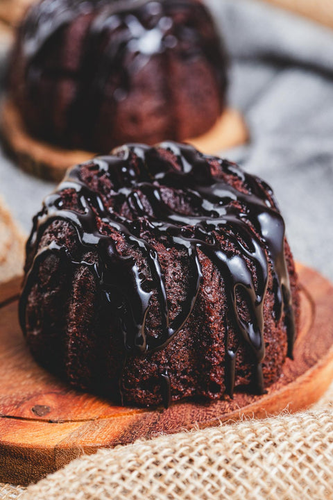 A chocolate bundt cake with chocolate glaze on top, served on a wooden plate.