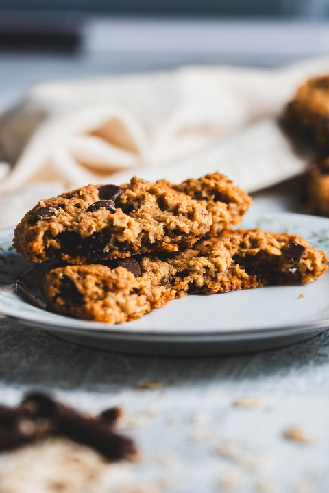 Close up of an oatmeal chocolate chip cookie broken open on a plate to show chocolate pieces and soft texture
