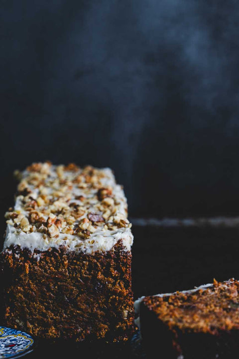 Carrot walnut loaf topped with creamy frosting and crushed walnuts displayed on a decorative plate.