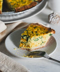 Slice of spinach cheddar quiche on a white plate with a bite taken out.