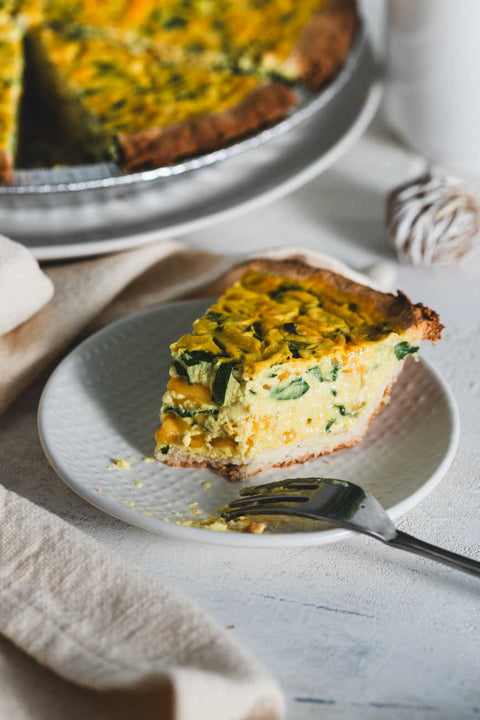 Slice of spinach cheddar quiche on a white plate with a bite taken out.