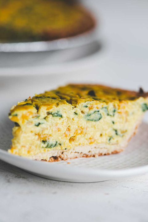 Close up of a slice of spinach cheddar quiche on a white plate.