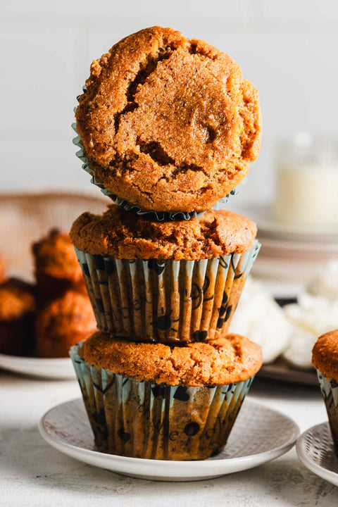 A stack of three golden-brown muffins on a white plate, with the top muffin balancing on its side.