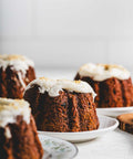 A photo showing several Mini Carrot Walnut Bundt cakes with a white glaze and crushed walnuts on top, placed on plates with a white background.