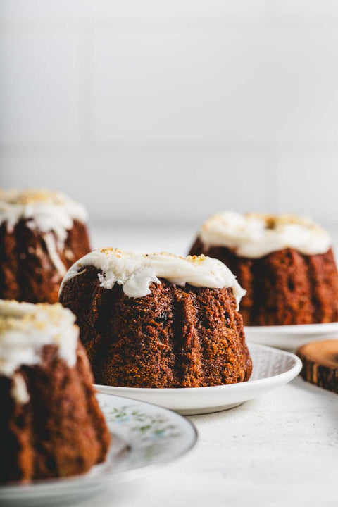 A photo showing several Mini Carrot Walnut Bundt cakes with a white glaze and crushed walnuts on top, placed on plates with a white background.