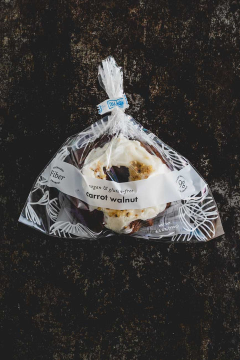 Top down view of a mini carrot walnut bundt cake with icing and crushed walnuts on top wrapped in a plastic bag