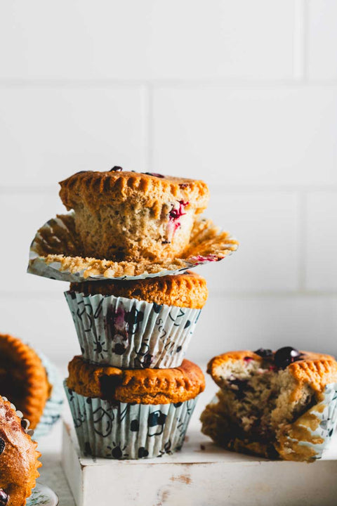 Stack of cinnamon pumpkin muffins with cranberries, showing one partially unwrapped muffin on top and a bitten muffin on the side, placed on a white surface.