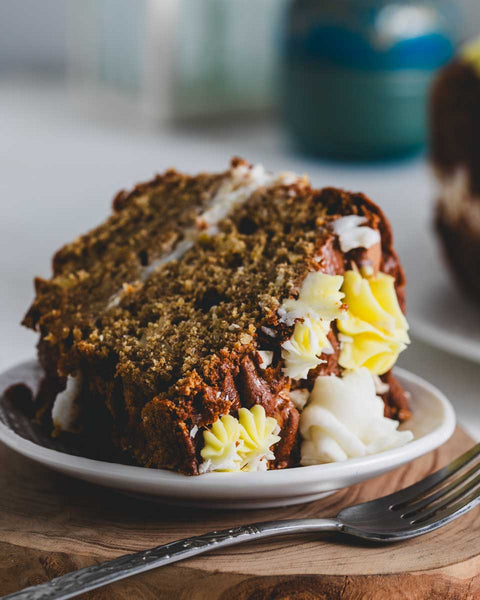 Close-up of a single slice of lemon almond bundt cake on a white plate. The slice shows the moist, dense texture of the cake with layers of white and yellow frosting.