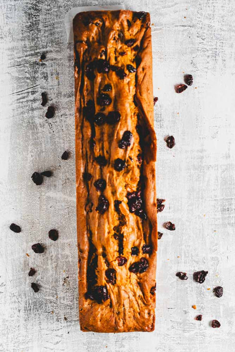 pumpkin loaf with cranberries in it and sprinkled around. A slice is cut off.