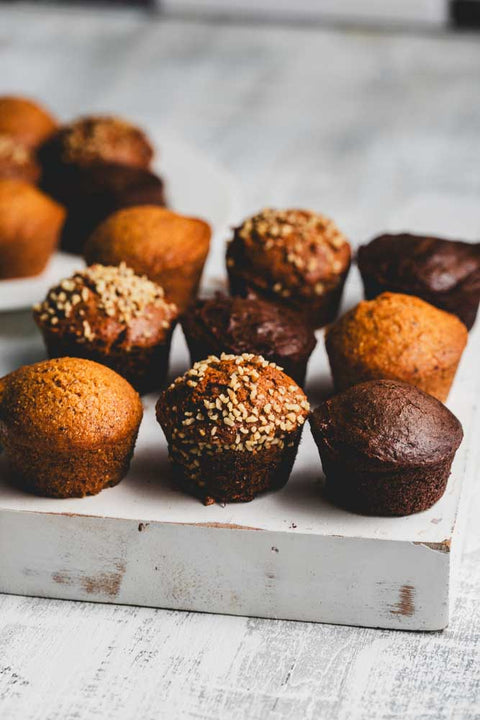 A variety of mini muffins on a white surface, with some muffins topped with nuts.