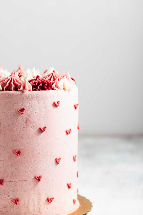 Close up of a pink velvet cake with pink frosting with decorative pink hearts and pink and white frosting decorations