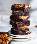 Stack of oatmeal brookies on a white plate with a single piece on the side and chocolate chunks scattered.