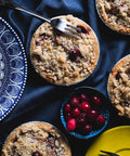 Mini cranberry apple pie with a crumb topping, served with a fork on a dark blue cloth, surrounded by fresh cranberries.