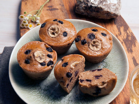 Plate of banana blueberry muffins set on a wooden board with chamomile flowers in the background.