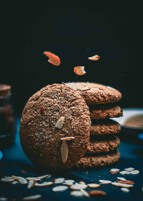 Stack of salted almond chocolate chip cookies with scattered almond slices, one cookie leaning against the stack.