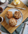 Two harvest muffins on a plate with coffee and butter on a wooden board.