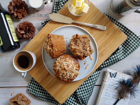Two harvest muffins on a plate with coffee and butter on a wooden board.