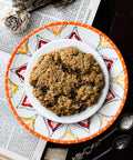 A single oatmeal raisin cookie on a colorful patterned plate, featuring vintage papers and spoons.