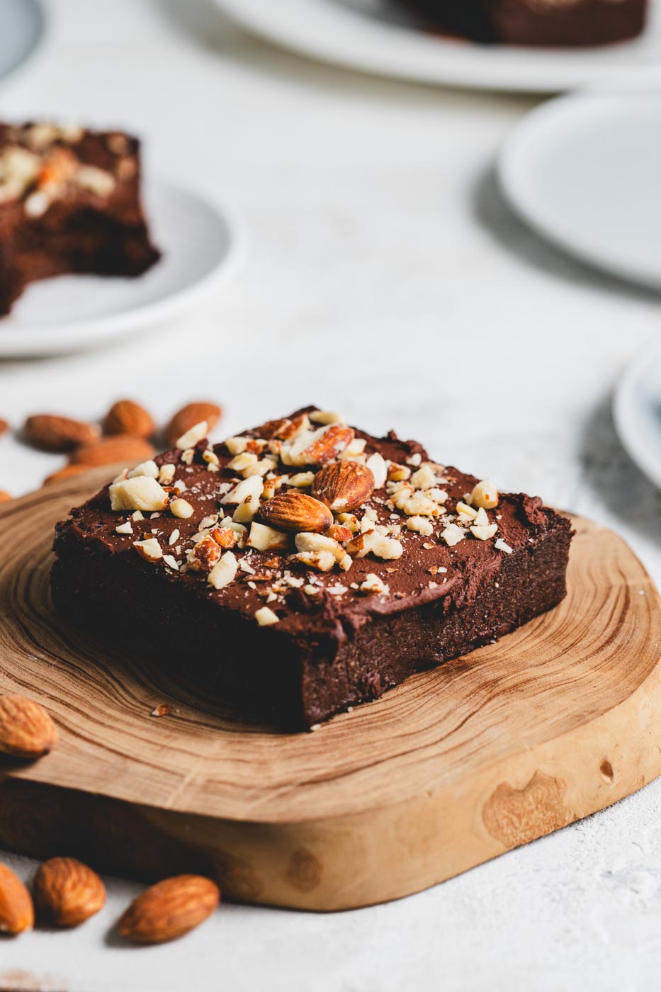 A sugar free keto brownie with a crushed almond topping on a wooden tray with almonds scattered around