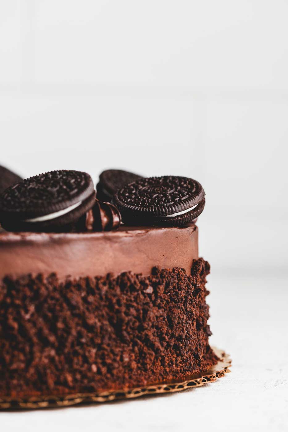 Aclose up side view of a chocolate frosted cake with chocolate frosting dollops and oreos as decoration, rolled in chocolate cake crumbs. 