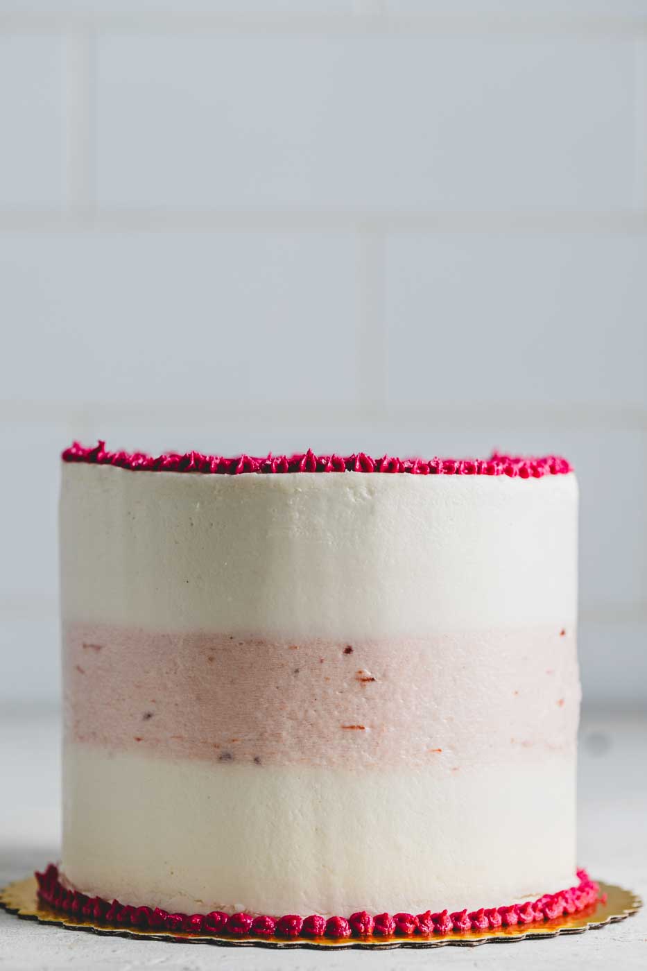 A side view of a cake with striped vanilla and strawberry frosting with bright pink frosting decorations 