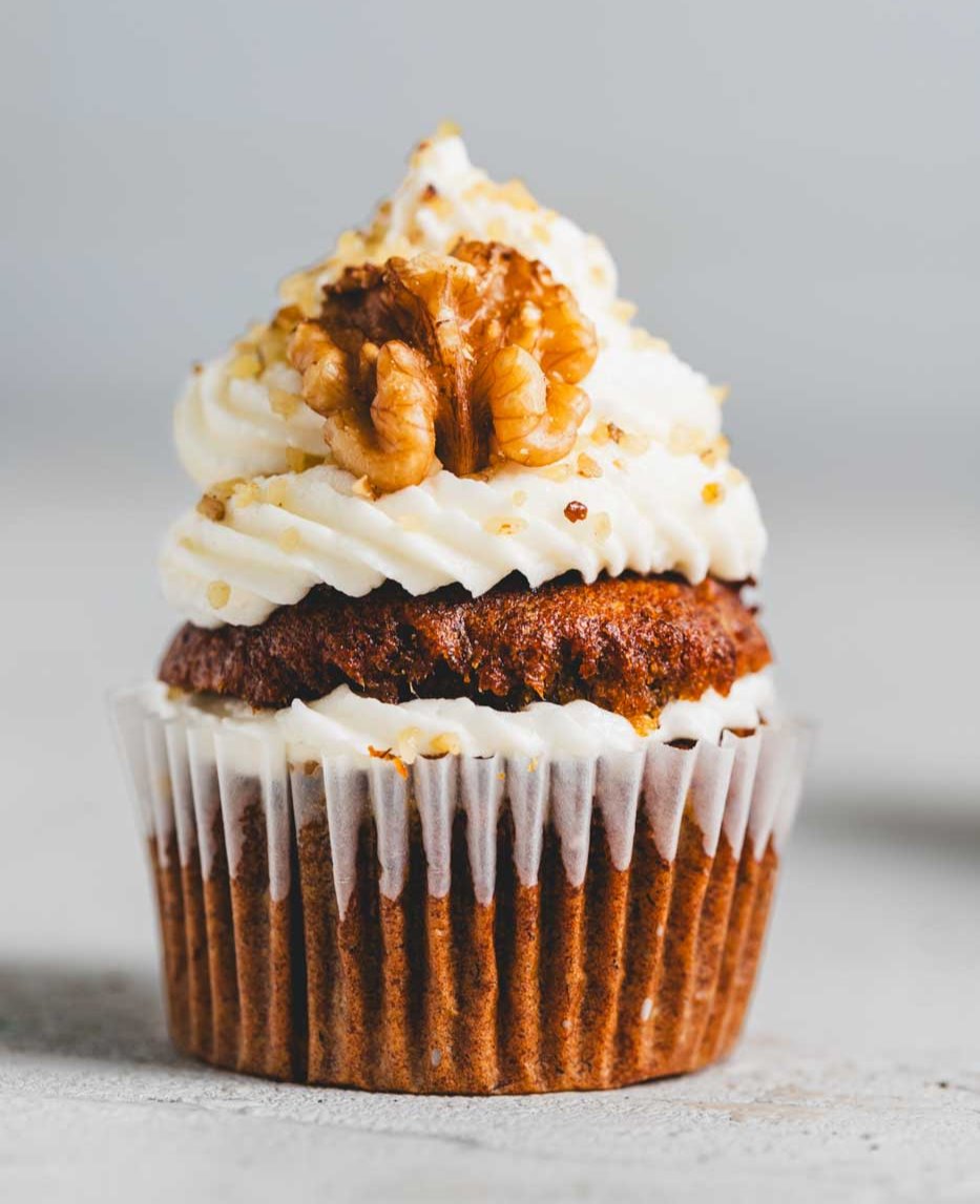 A close up of a banana walnut cupcake with vanilla icing and a walnut garnish