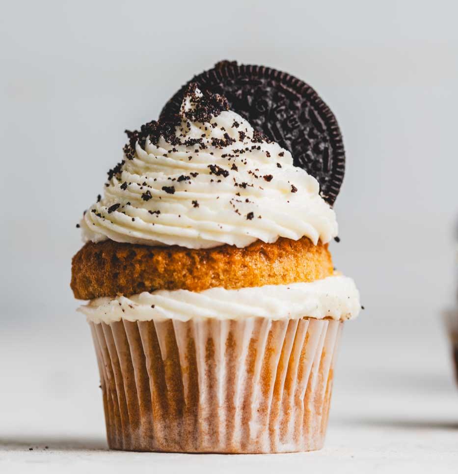 A close up of a vanilla cupcake with vanilla icing and oreo cookie on top