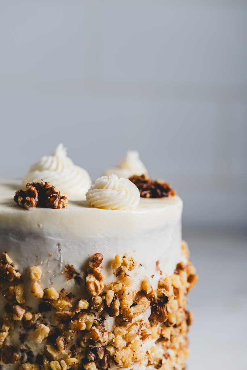 close up of banana walnut cake with vanilla icing and crushed walnut decoration