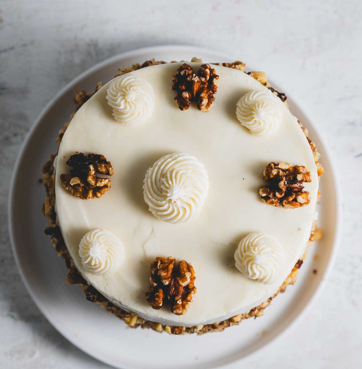 Banana walnut cake seen from above with decorative swirls of frosting and whole walnuts, rolled in crushed walnuts.