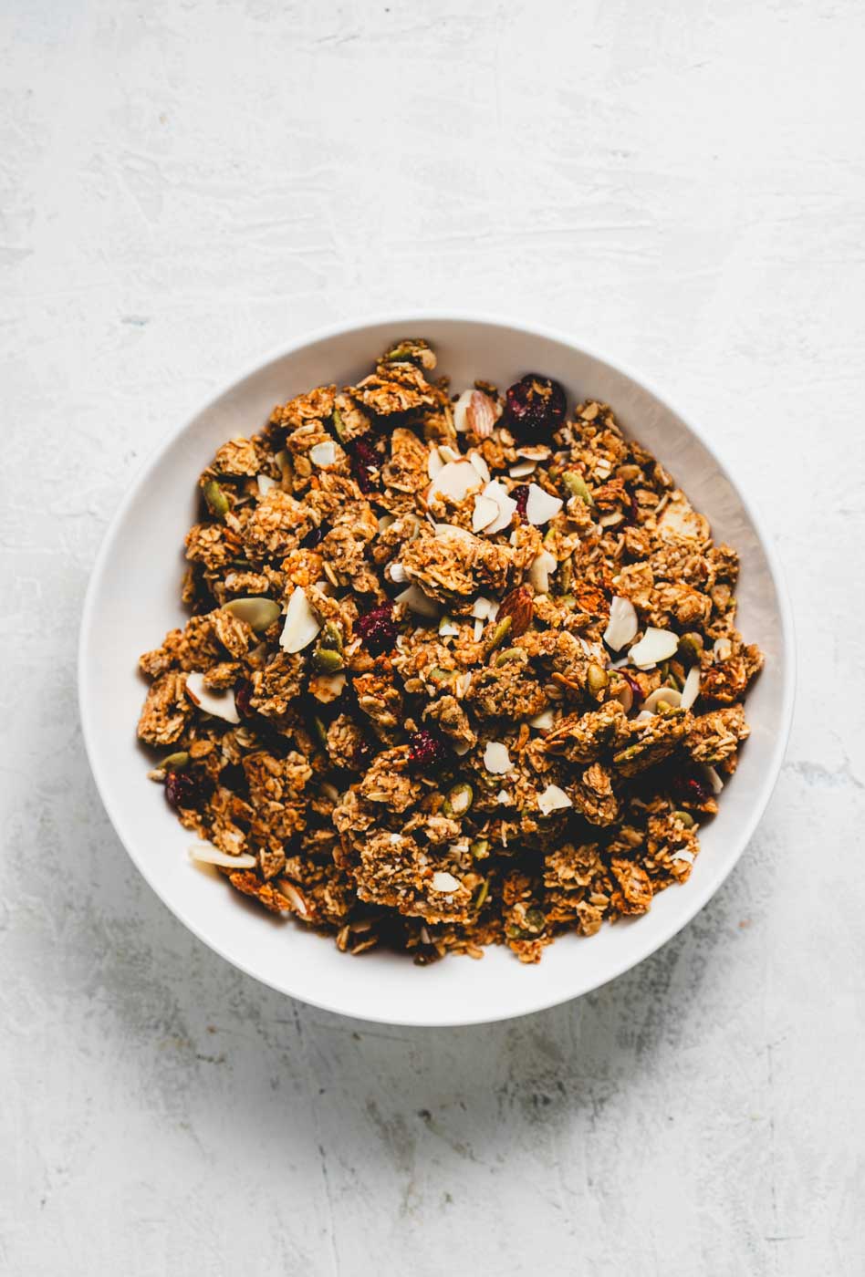 White bowl of granola with oats, pumpkin seeds, almonds, and cranberries