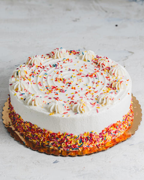 Vanilla birthday cake with white frosting amd colorful sprinkles.