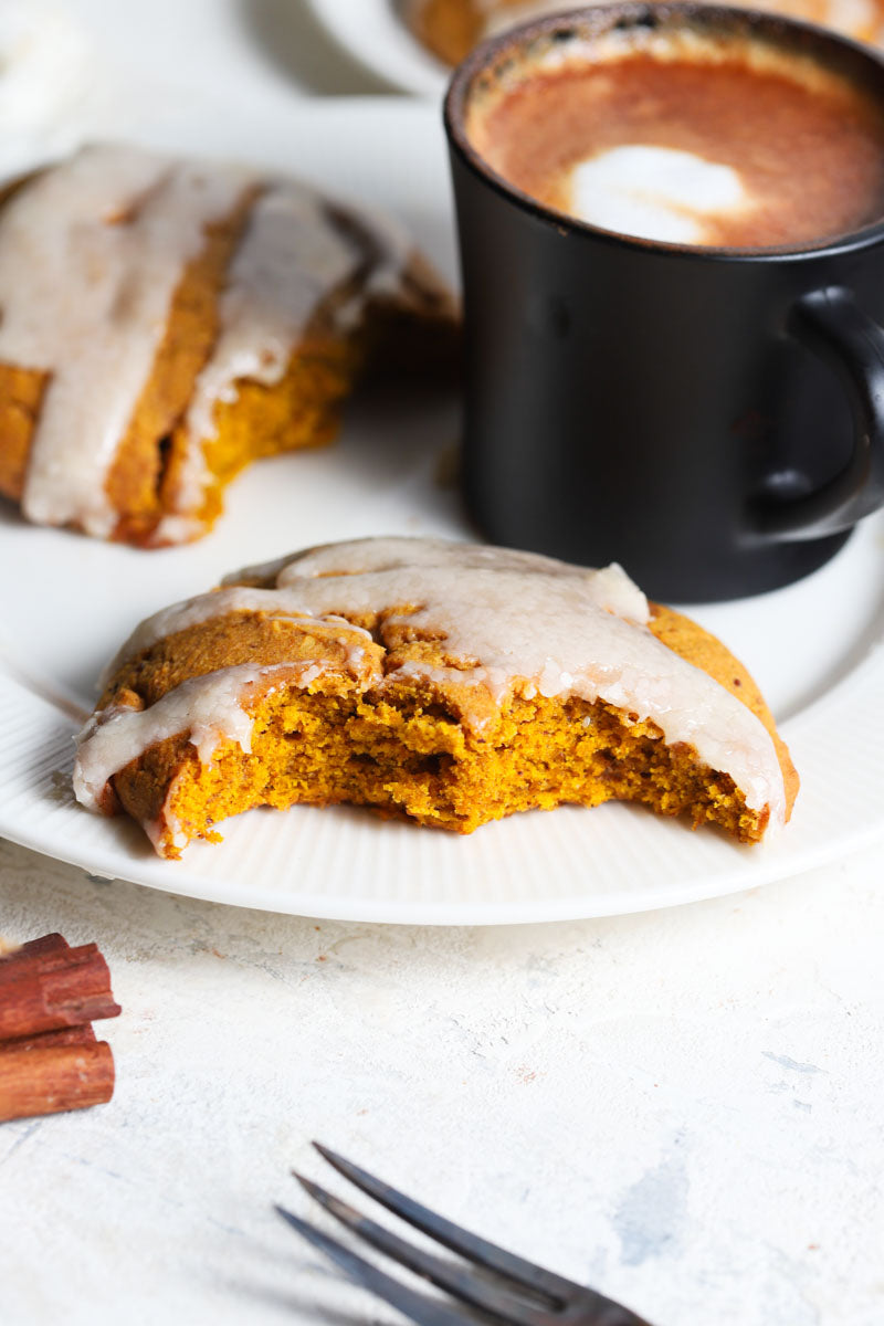 Pumpkin cheesecake scone with a bite taken out on a plate with a mug of coffee.