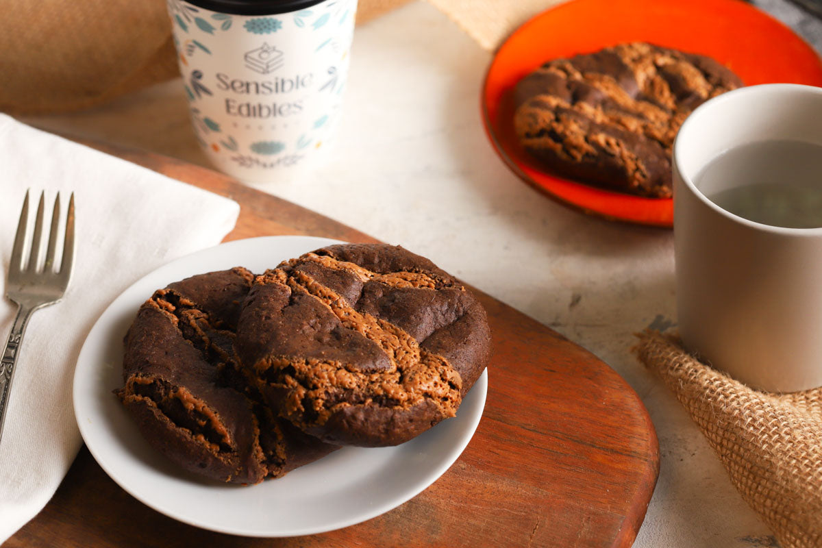 Chocolate chia cookies on a plate with a mug and a Sensible Edibles coffee cup.